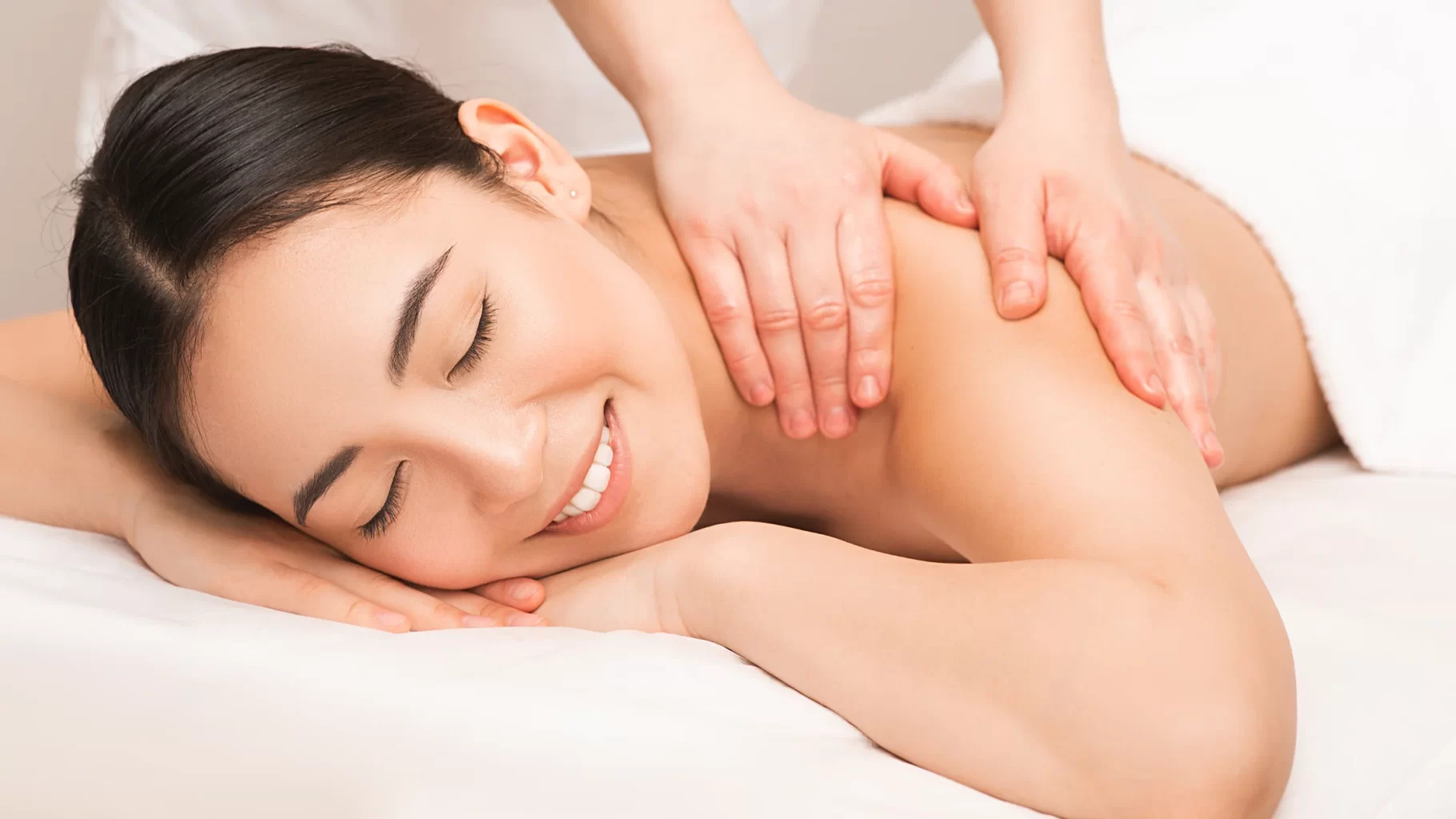 Smiling woman enjoying a relaxing back massage on white spa bed during wellness treatment session