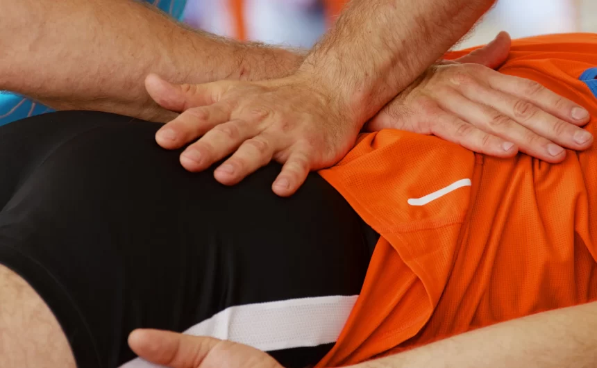 Physical therapist applying manual pressure to athlete’s hip and lower back during recovery