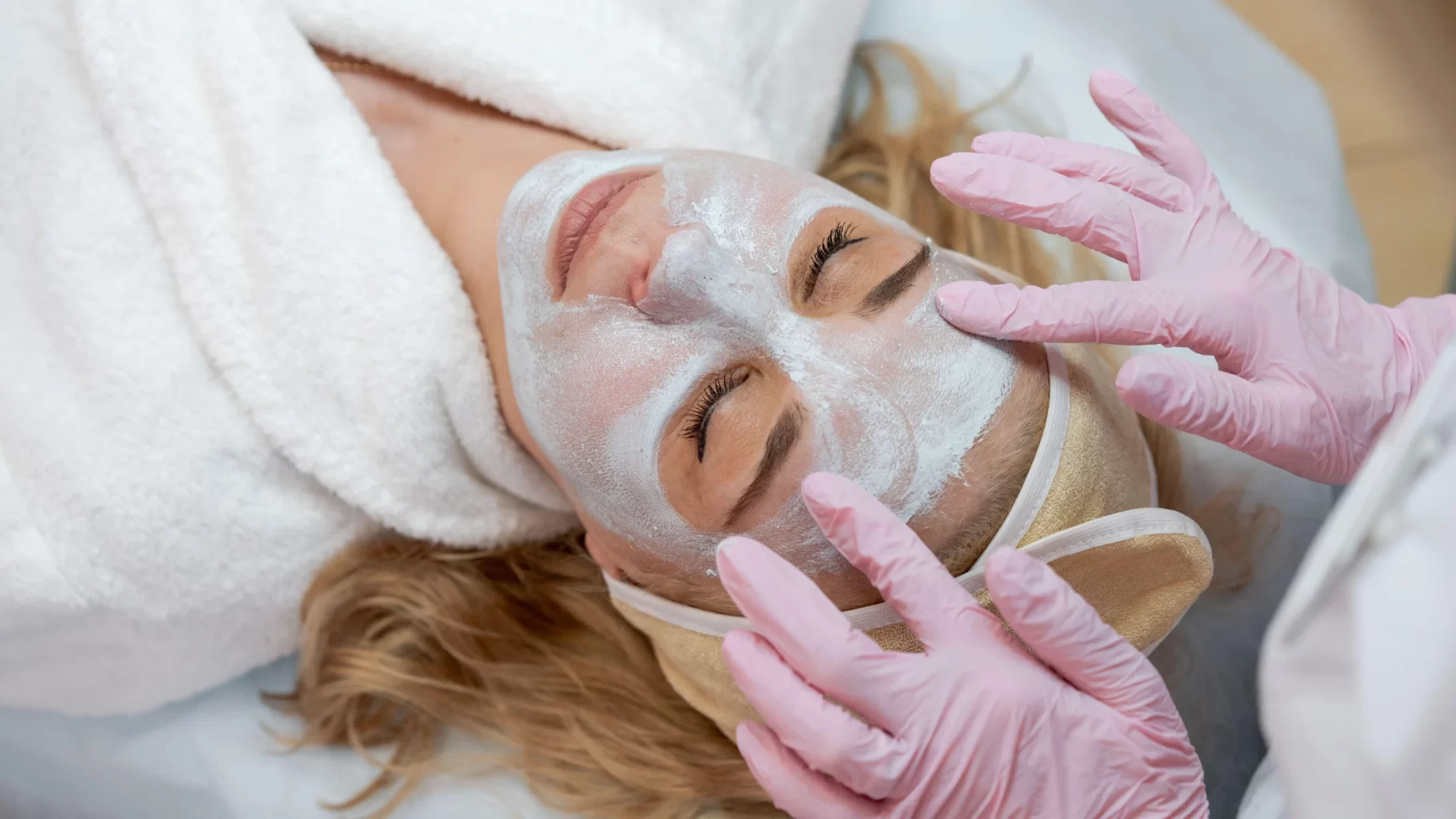 Esthetician applying facial mask with pink gloves during relaxing spa skincare treatment session