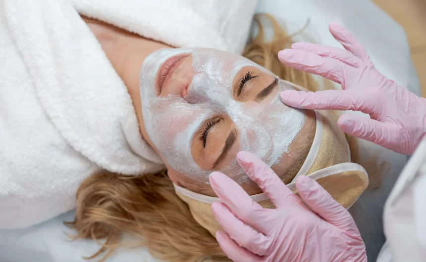 Esthetician applying facial mask with pink gloves during relaxing spa skincare treatment session