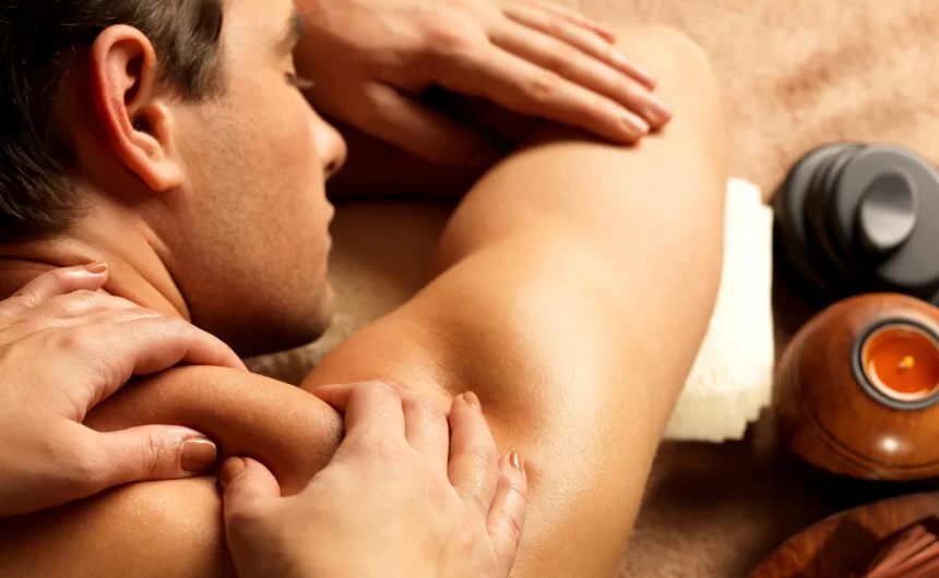 Man receiving shoulder and upper back massage with spa candle and warm therapy tools nearby