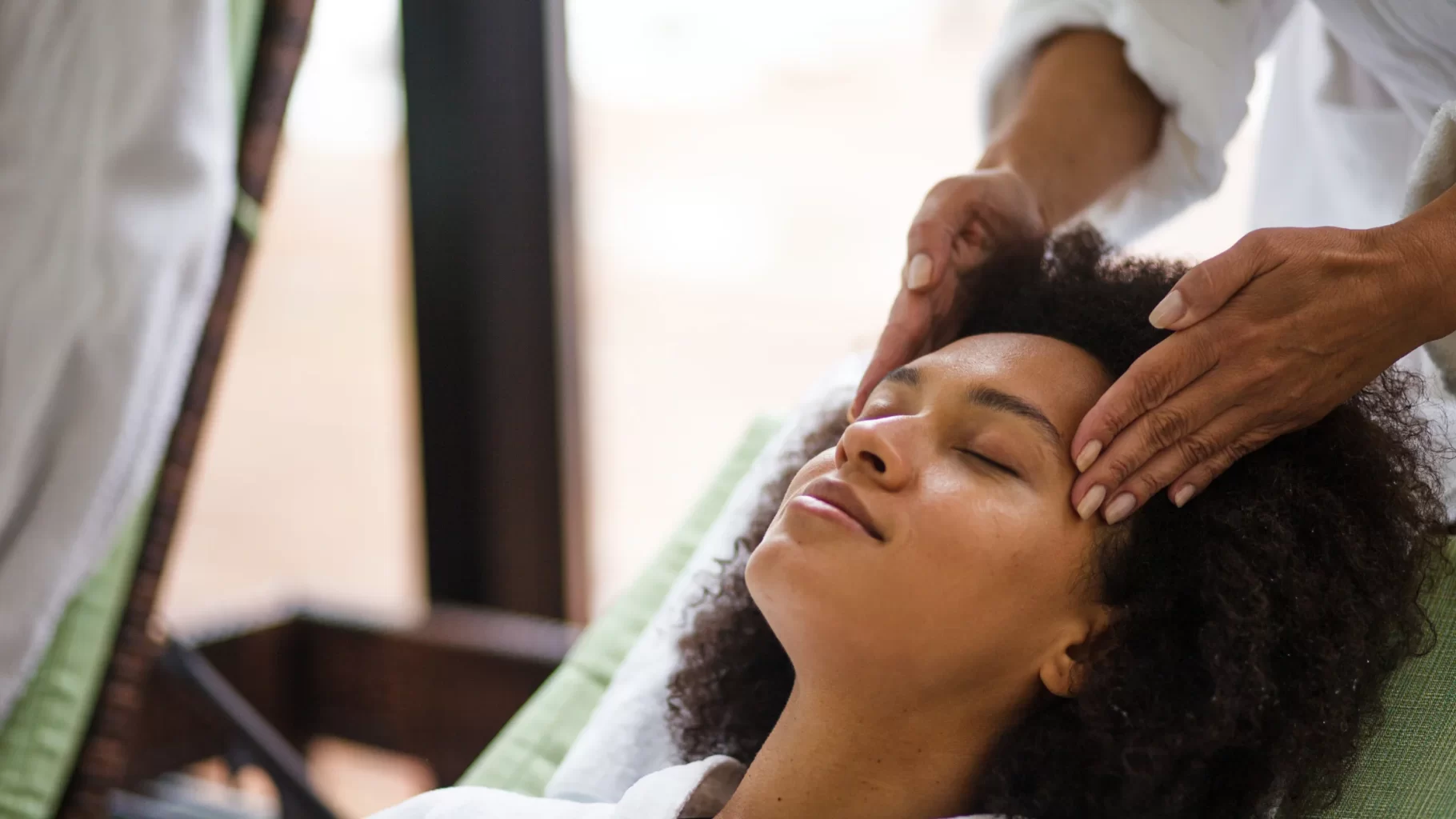 Woman relaxing with eyes closed during calming scalp and facial massage at a wellness spa visit