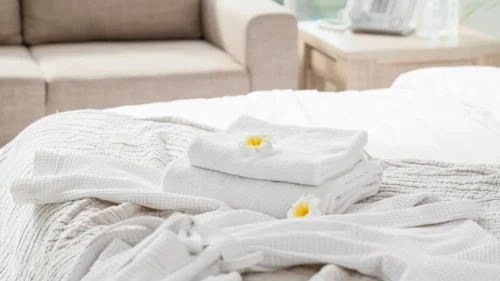 Bright spa treatment bed with folded white towels, robes, and flowers arranged for a relaxing wellness visit.