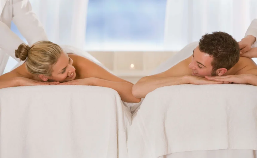 Couple receiving side-by-side massage treatments on spa tables in a bright and peaceful wellness room.