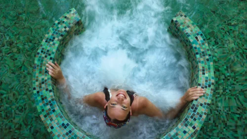 Woman relaxes in a bubbling spa hot tub surrounded by mosaic tiles, enjoying a calm wellness moment.