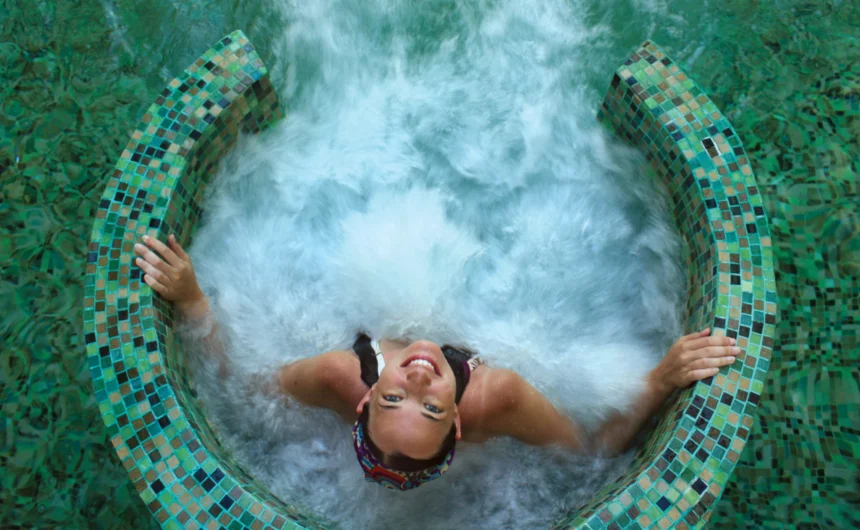Woman relaxes in a bubbling spa hot tub surrounded by mosaic tiles, enjoying a calm wellness moment.