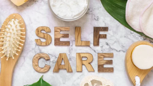 Self care message displayed with wooden letters among skincare tools, brushes, cream, and spa items.