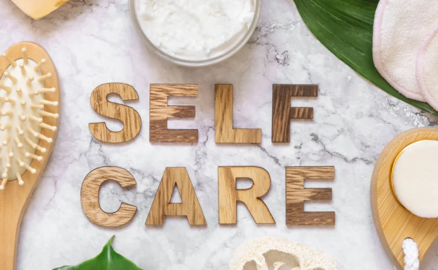 Self care message displayed with wooden letters among skincare tools, brushes, cream, and spa items.